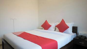 A hotel room with a bed, a bedside table with a telephone, and a wall socket.