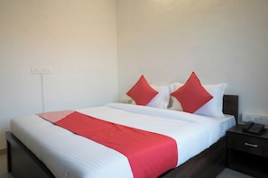 Quarto de hotel com uma cama, mesa de cabeceira com telefone e tomada na parede.