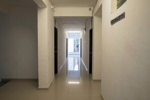 Corredor com portas em ambos os lados, que leva a uma área iluminada com vista para prédios lá fora.