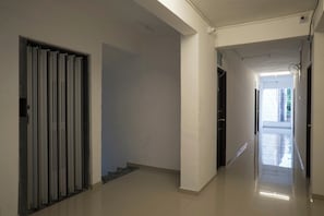 Corredor com porta de metal, escada e porta que dá para um quarto iluminado.
