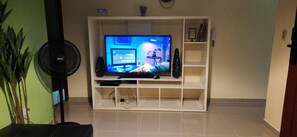 Uma sala de estar com televisão, caixas de som e ventilador.