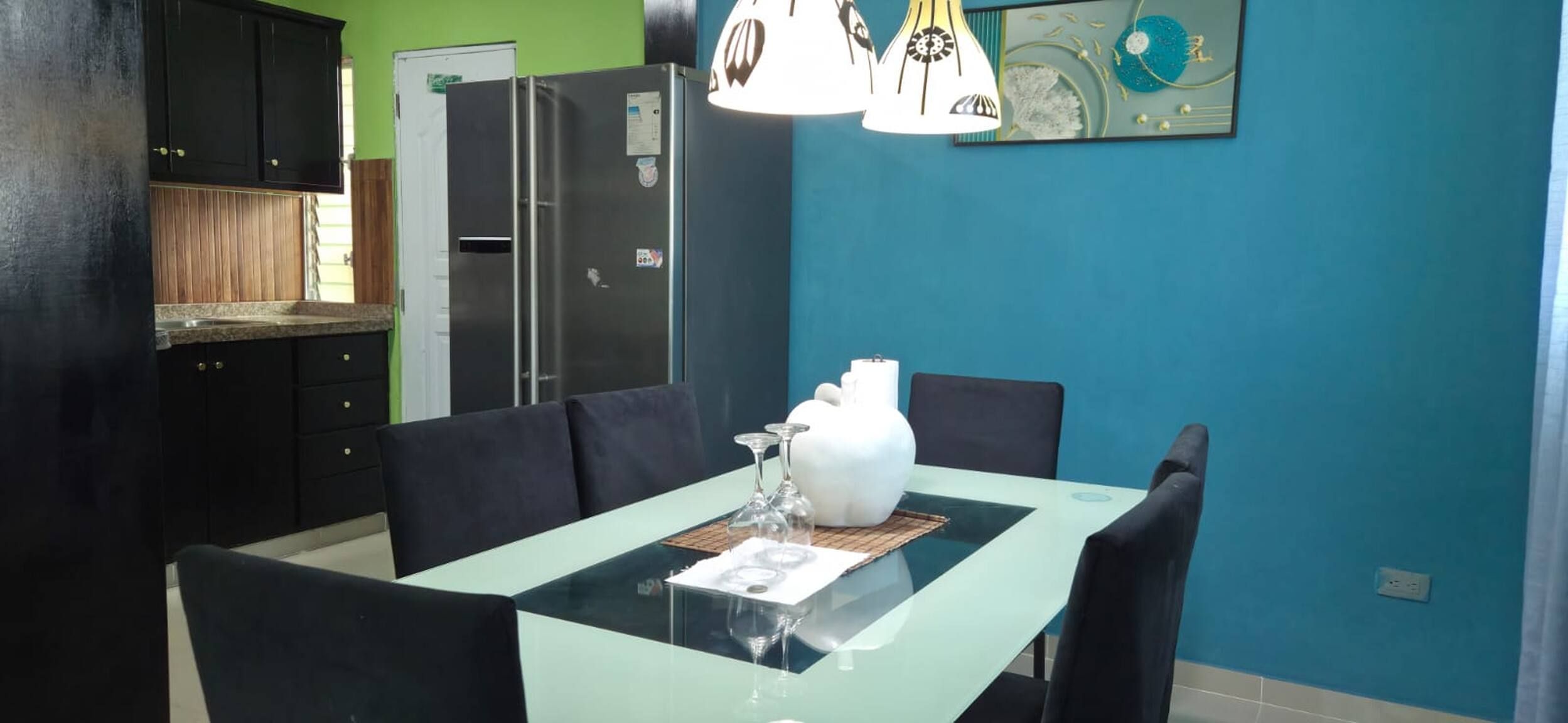 Un comedor con una mesa dispuesta para dos personas, un jarrón blanco y un vaso.