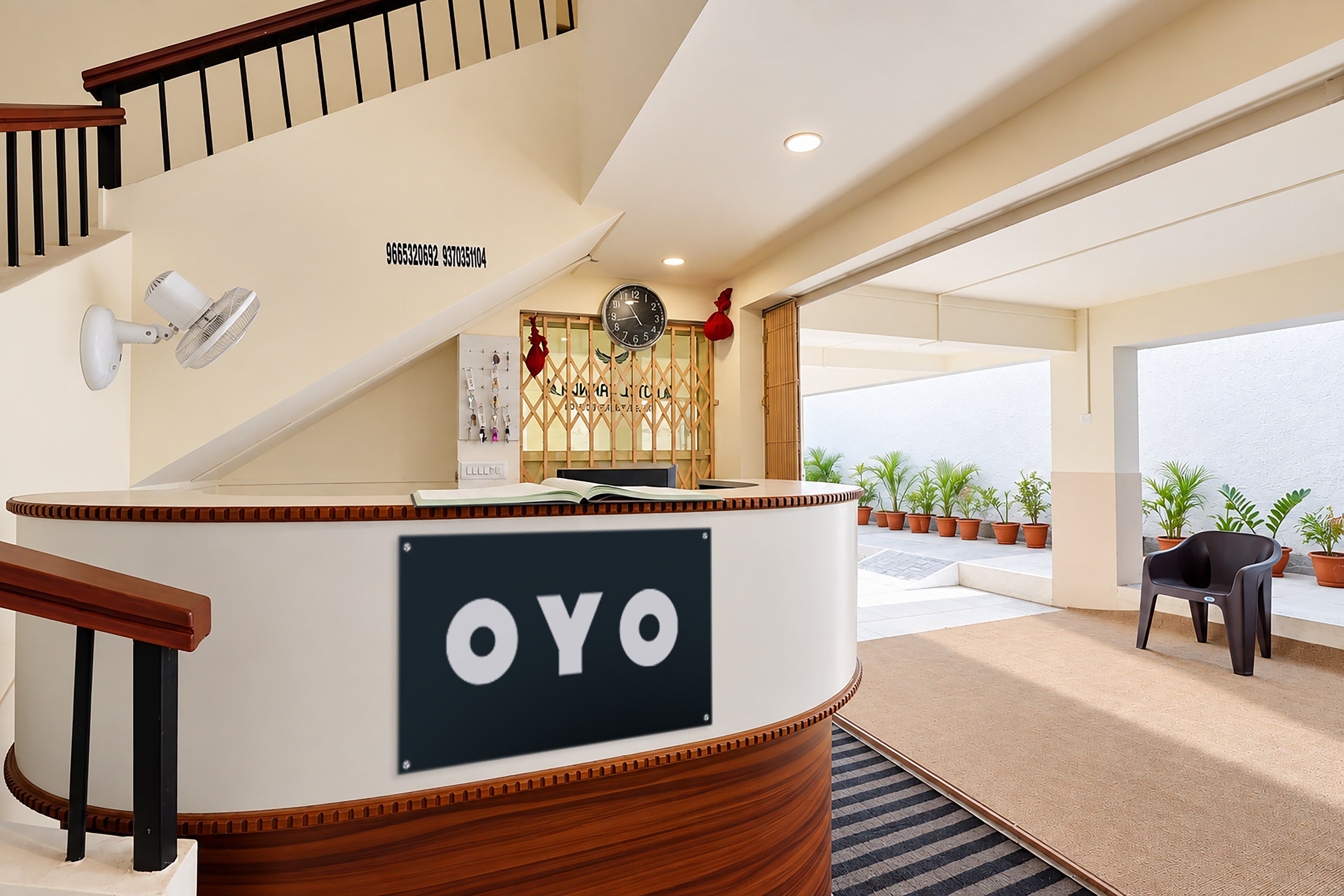 Et receptionsområde med en træreception, skilt med 'OYO', et ur og udsigt udendørs gennem store vinduer.