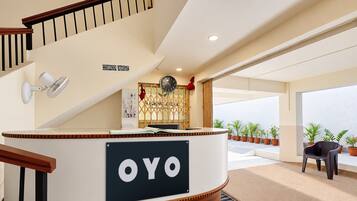 Et receptionsområde med en træreception, skilt med 'OYO', et ur og udsigt udendørs gennem store vinduer.