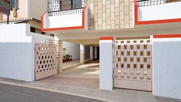 Entrada fechada por grades para um edifício residencial, com fachada revestida de azulejos e uma varanda com guarda-corpo de metal.