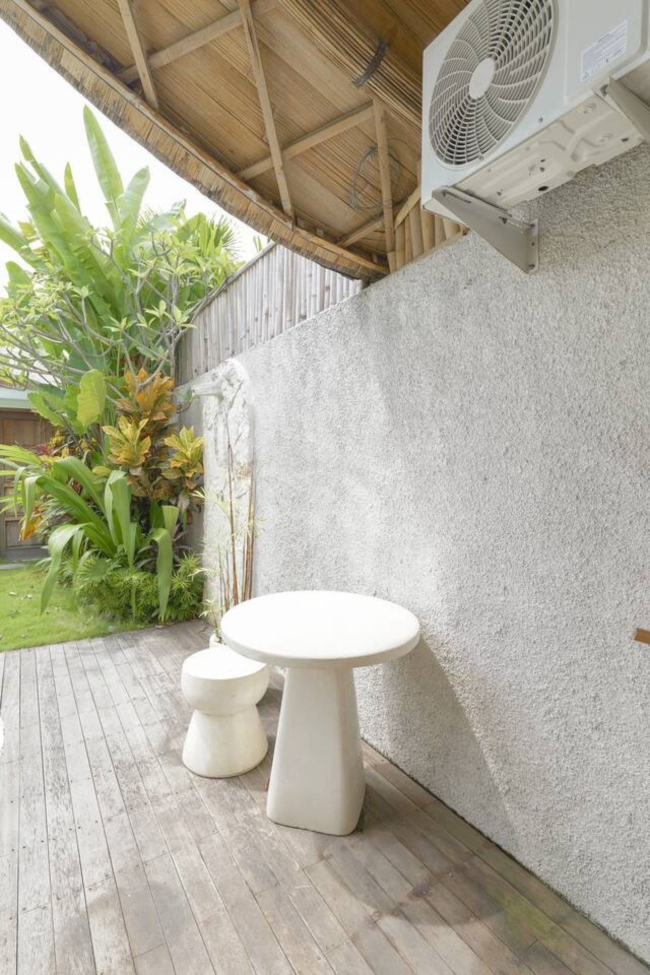 An outdoor patio with a round table and two stools, a concrete wall, and a fan mounted on the wall.
