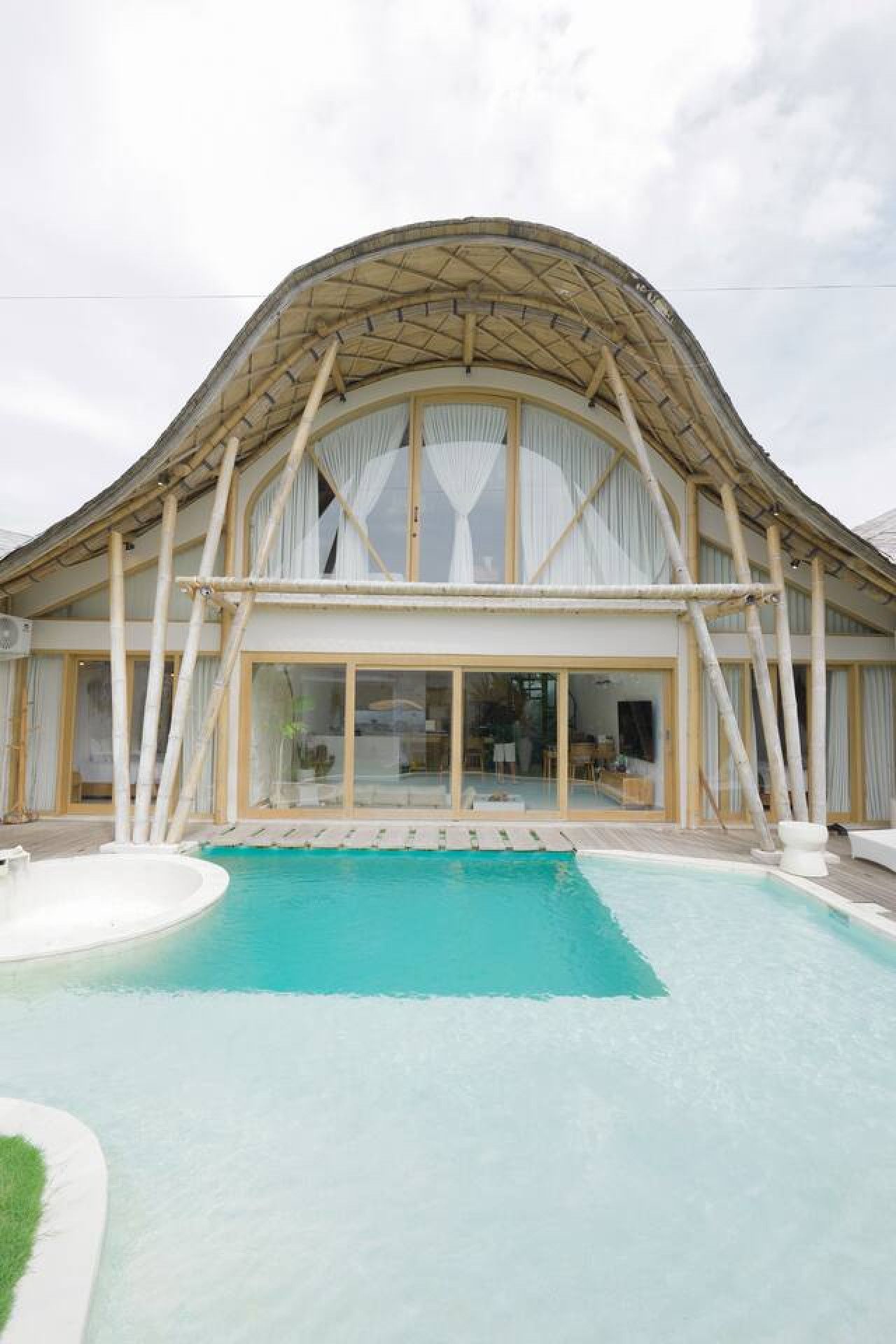 A modern villa with a large swimming pool, large windows, and a curved roof structure.
