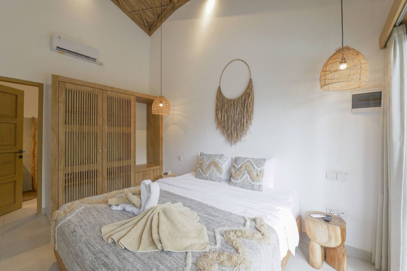 A bedroom with a bed, a wooden wardrobe, a hanging light fixture, and a small wooden side table.