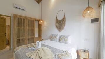 A bedroom with a bed, a wooden wardrobe, a hanging light fixture, and a small wooden side table.