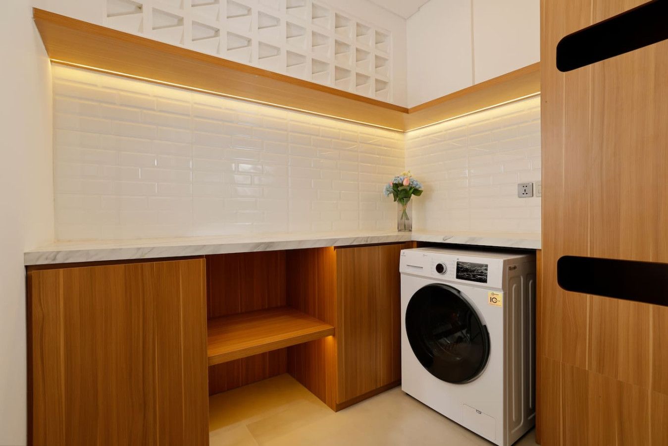 A compact laundry room with a washing machine, wooden cabinetry, and a white tiled backsplash.