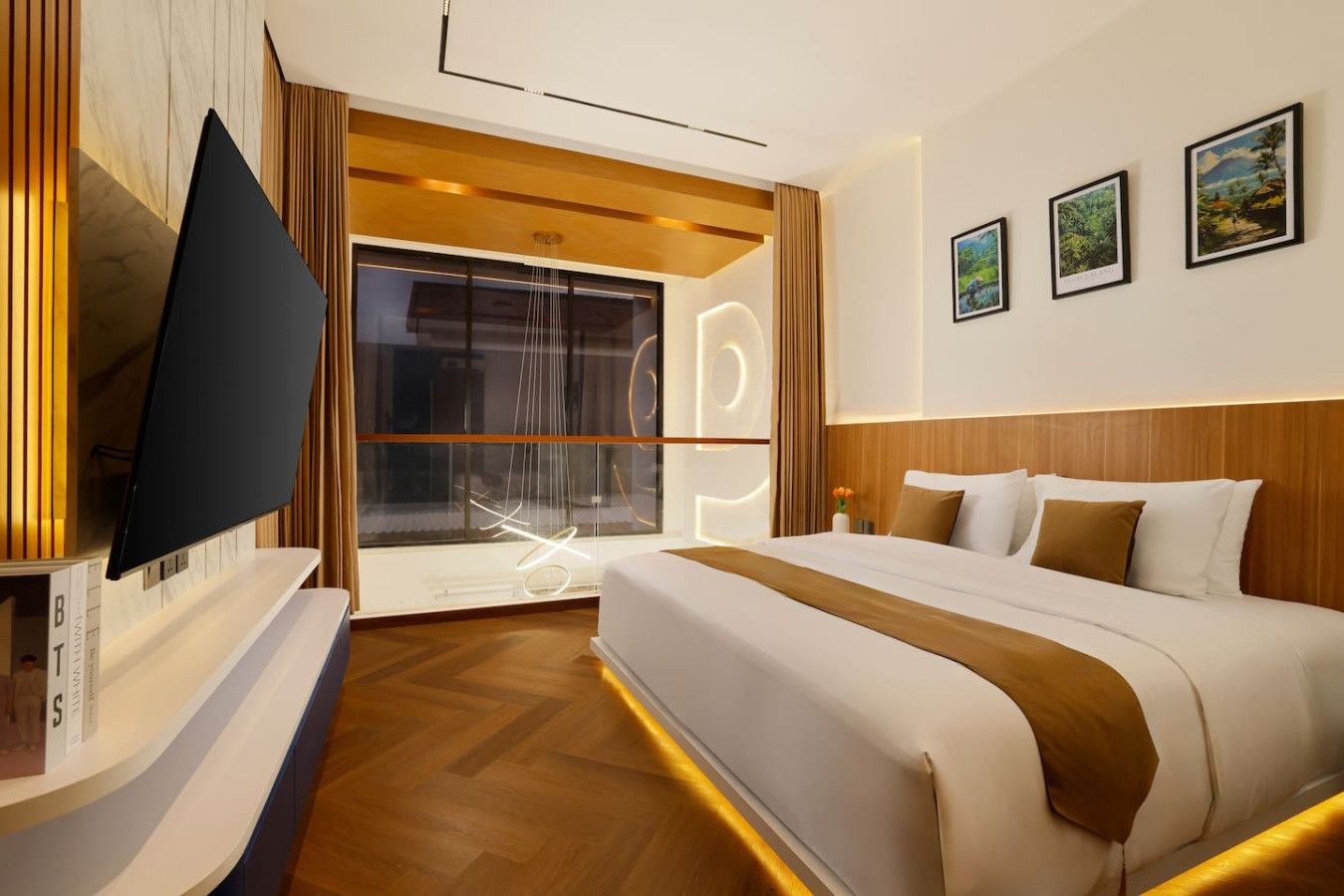 A modern hotel room with a large bed, a flat-screen TV, a large window with curtains, and framed artwork on the wall.