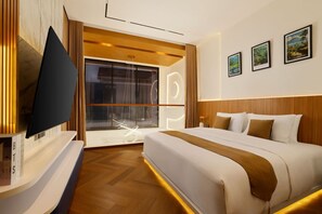 Et hotelværelse med en stor seng, et fladskærms-tv, et vindue med gardiner og billedkunst på væggen.