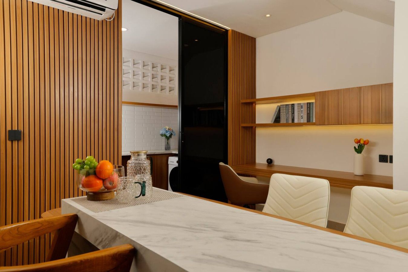 A modern dining area with a marble table, wooden paneling, and a bookshelf with books.