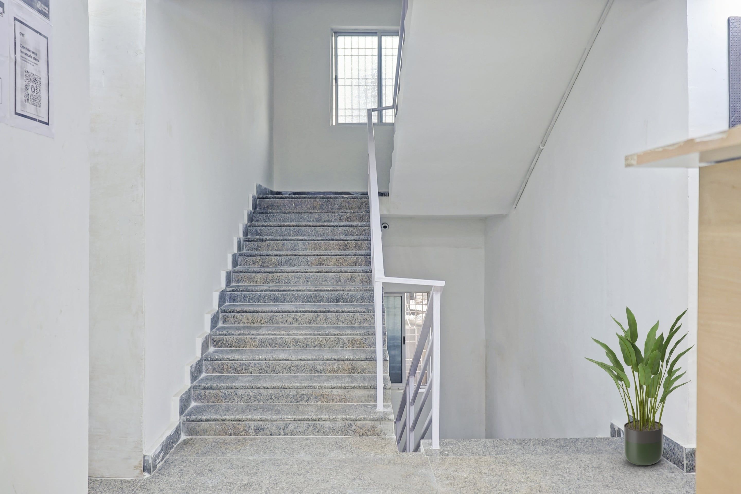 A staircase with a handrail, a small window at the top, and a potted plant on the landing.