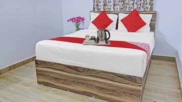 A neatly made bed with a wooden headboard, a red throw blanket, and a tray with a kettle and cups.