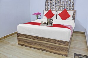 Una cama bien hecha con cabecera de madera, una manta roja y una bandeja con hervidor y tazas.