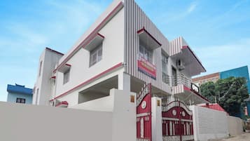 Un hotel moderno con una fachada destacada en rojo y blanco, una entrada protegida por una reja y un cielo azul claro al fondo.