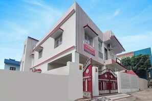 Un hotel moderno con una fachada destacada en rojo y blanco, una entrada protegida por una reja y un cielo azul claro al fondo.
