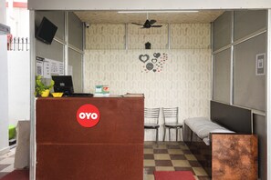 Zona de recepción con mostrador, sillas, cama, ventilador de techo y reloj de pared.