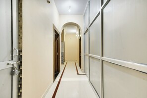 Un pasillo con suelo de baldosas, una puerta de madera y una pared blanca con una cámara de seguridad.