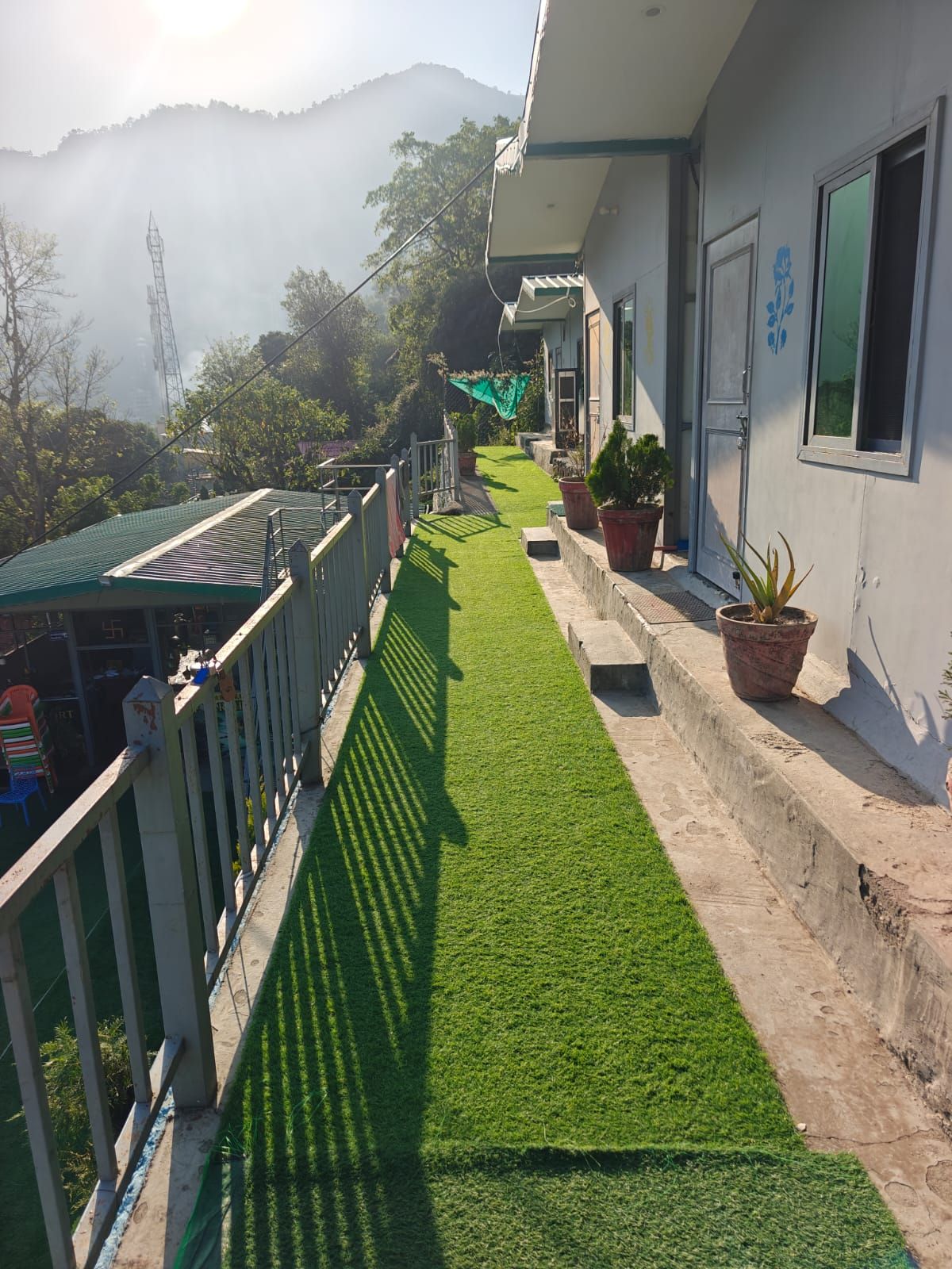 A residential building with a green artificial lawn, potted plants, and a view of a mountain.