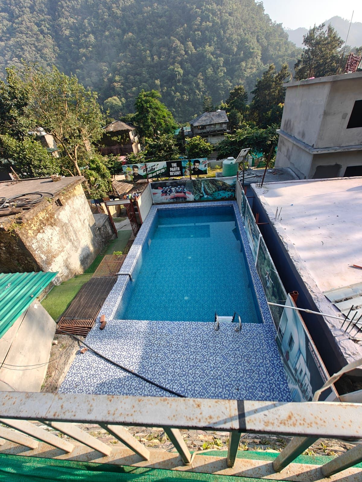 A rectangular swimming pool with a tiled deck, surrounded by a metal railing.