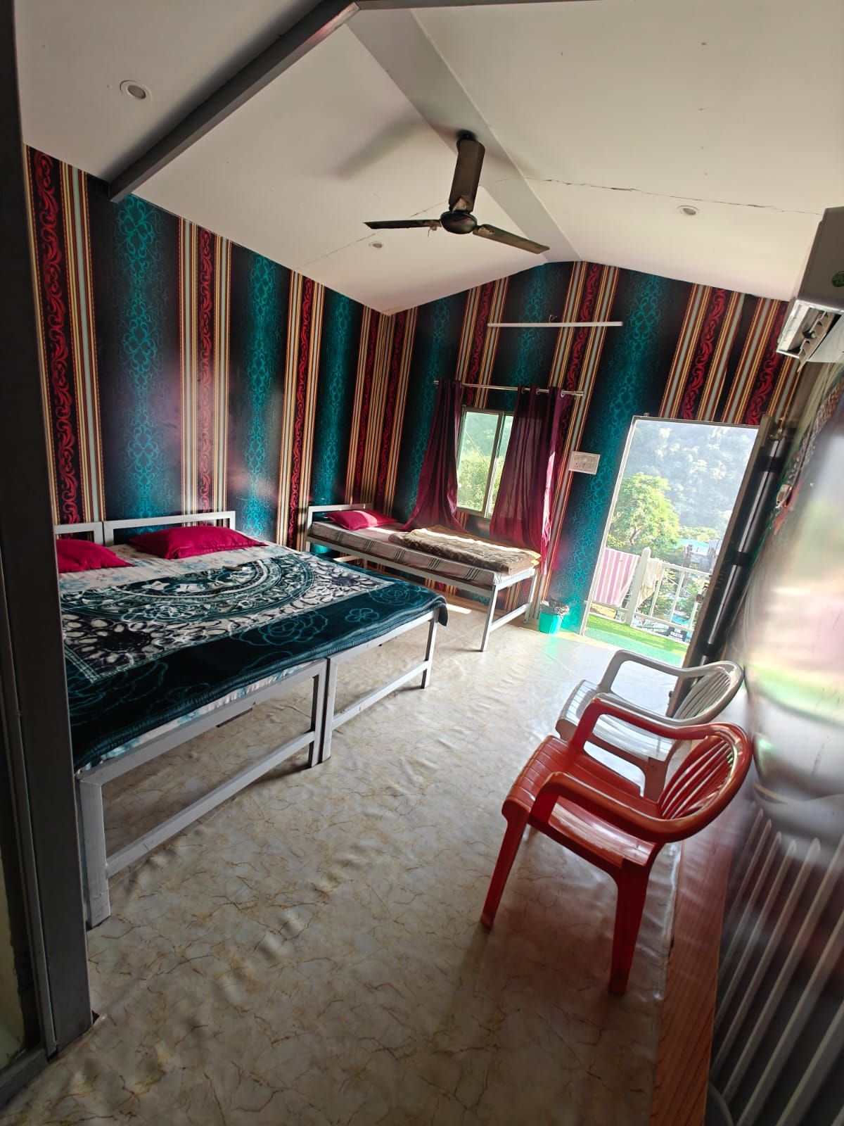 A room with two beds, a ceiling fan, a window with curtains, and a red chair.