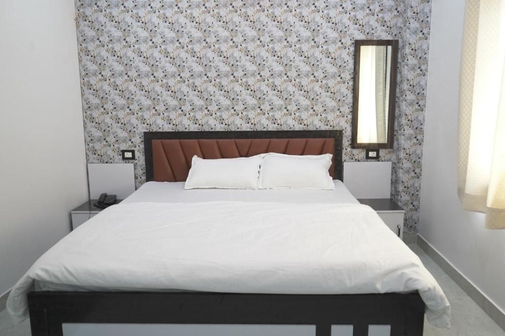 Een enkel bed met een houten hoofdbord, wit beddengoed en een nachtkastje met een telefoon.