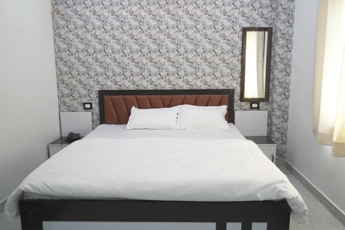 Un lit simple avec une tête de lit en bois, une literie blanche et une table de chevet avec un téléphone.