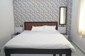 Un lit simple avec une tête de lit en bois, une literie blanche et une table de chevet avec un téléphone.
