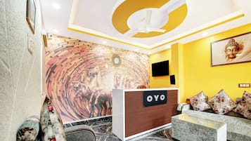 A reception area with a reception desk labeled 'OYO,' a wall mural, a Buddha statue, and a sofa with floral cushions.
