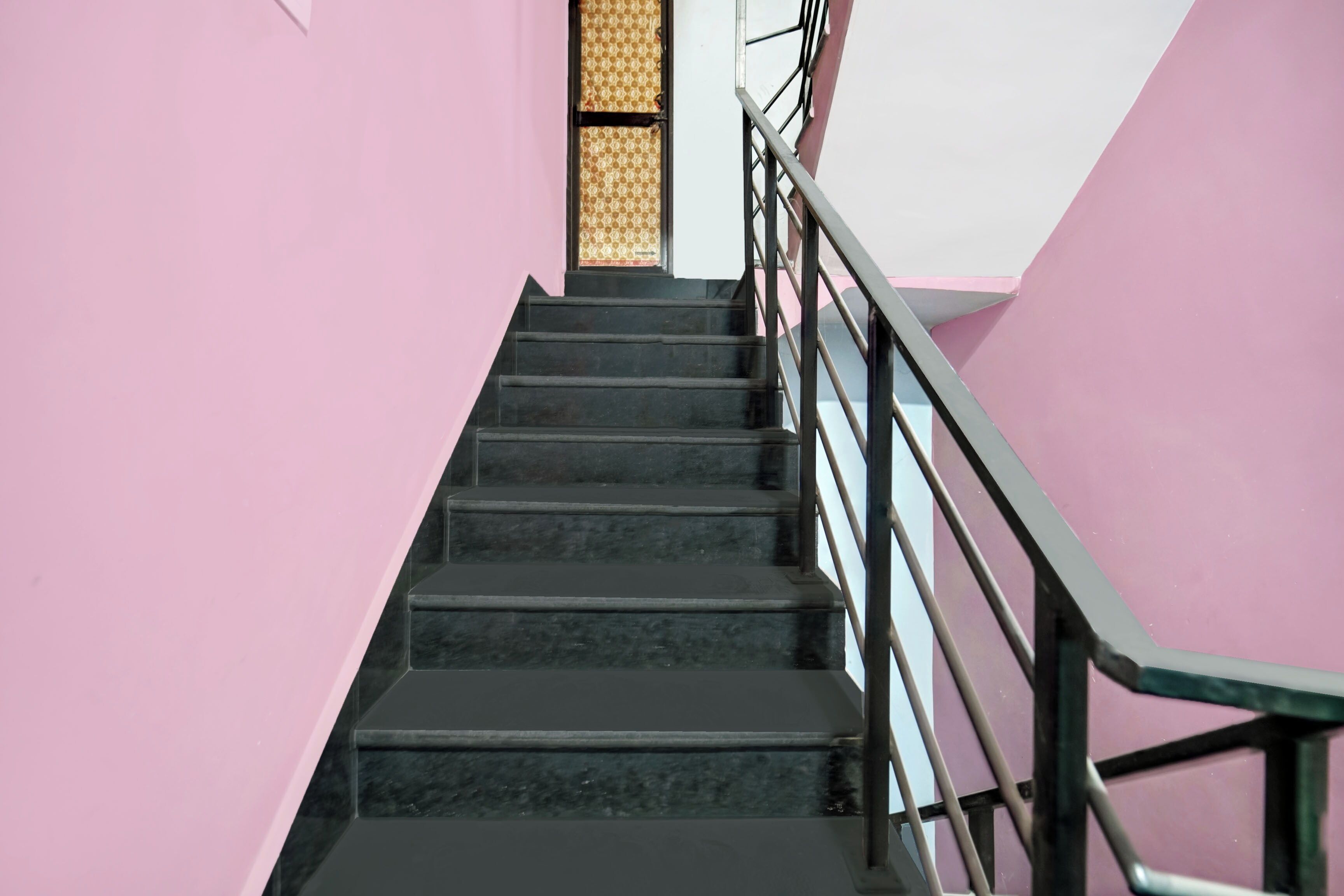 A staircase with black steps and a metal handrail, leading to a door with a patterned glass panel.
