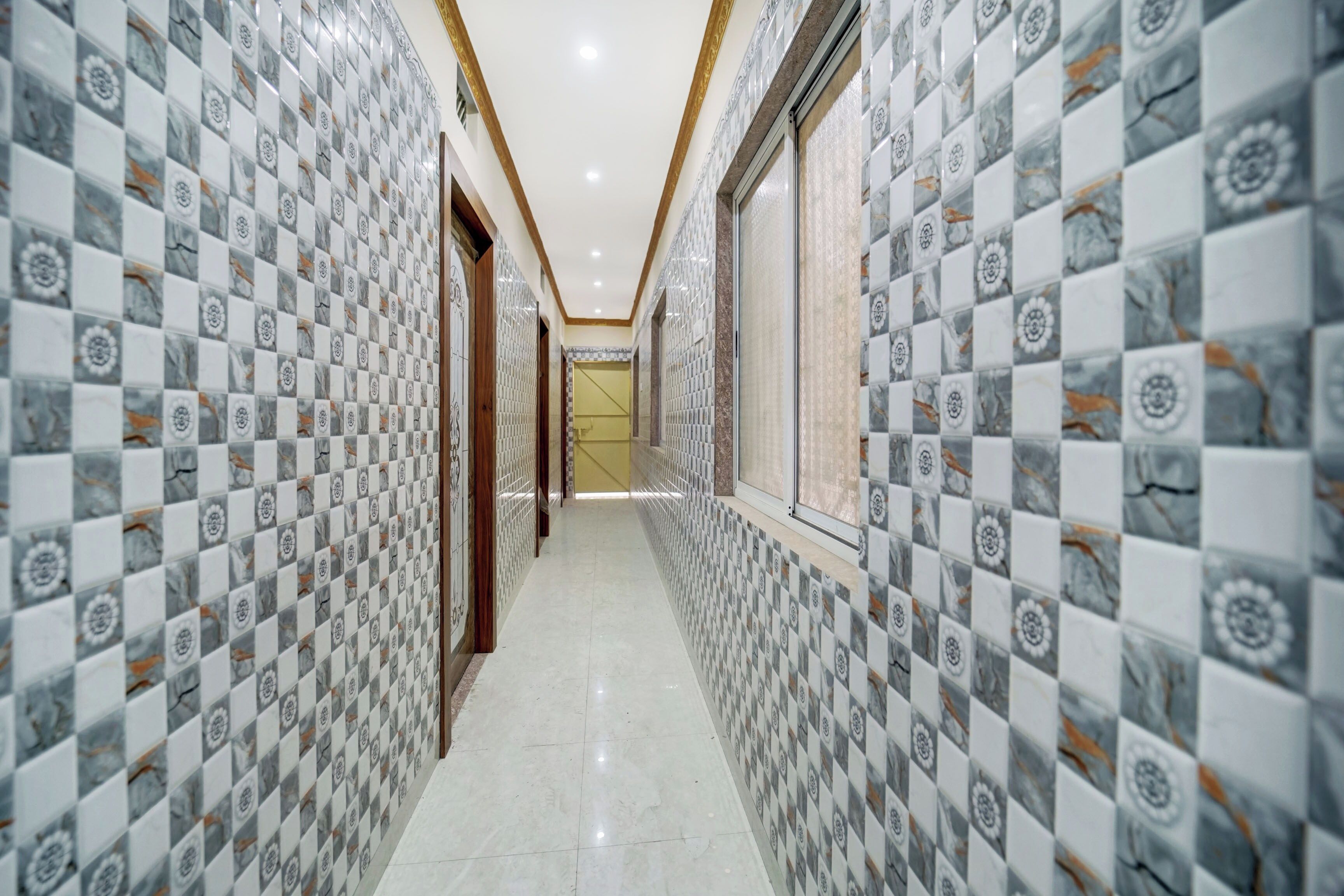 A corridor with patterned tiles on the walls and a tiled floor, leading to a door at the end.