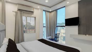 Habitación de hotel con cama, televisor de pantalla plana montado en la pared, ventana con cortinas y vista al exterior.
