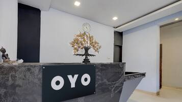 Una mesa de recepción con un cartel que dice 'OYO' y un árbol decorativo con hojas.