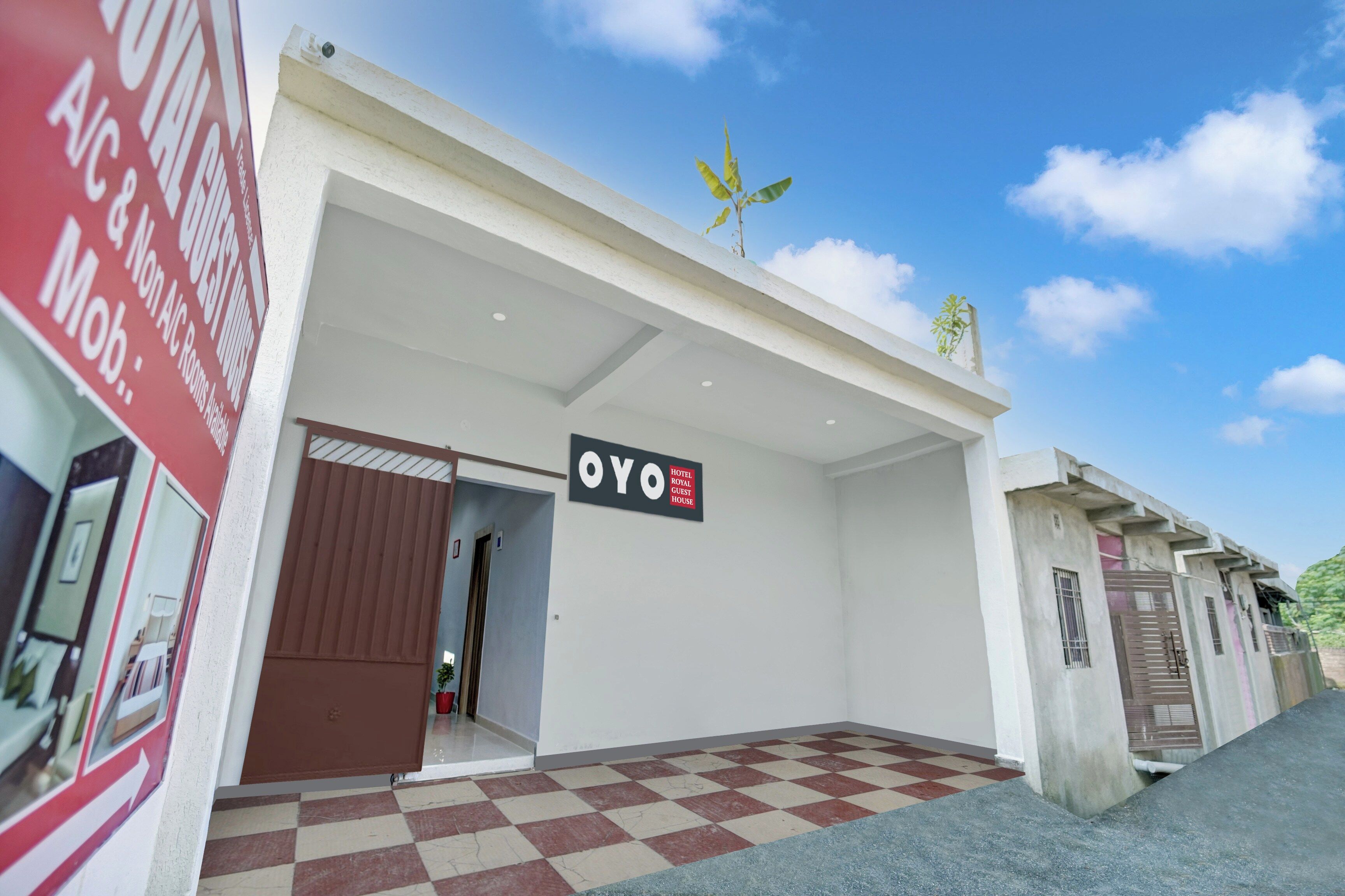 A hotel entrance with a checkered floor, a sign reading 'OYO HOTEL ROYAL GUEST HOUSE,' and a clear blue sky above.
