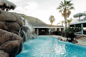 En pool med et vandfald, omgivet af sten og palmer.