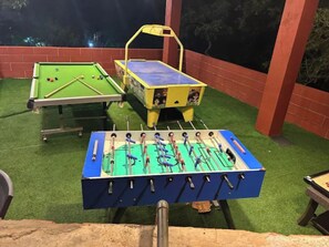 Mesa de sinuca, mesa de futebol de mesa e mesa de pingue-pongue em ambiente externo.
