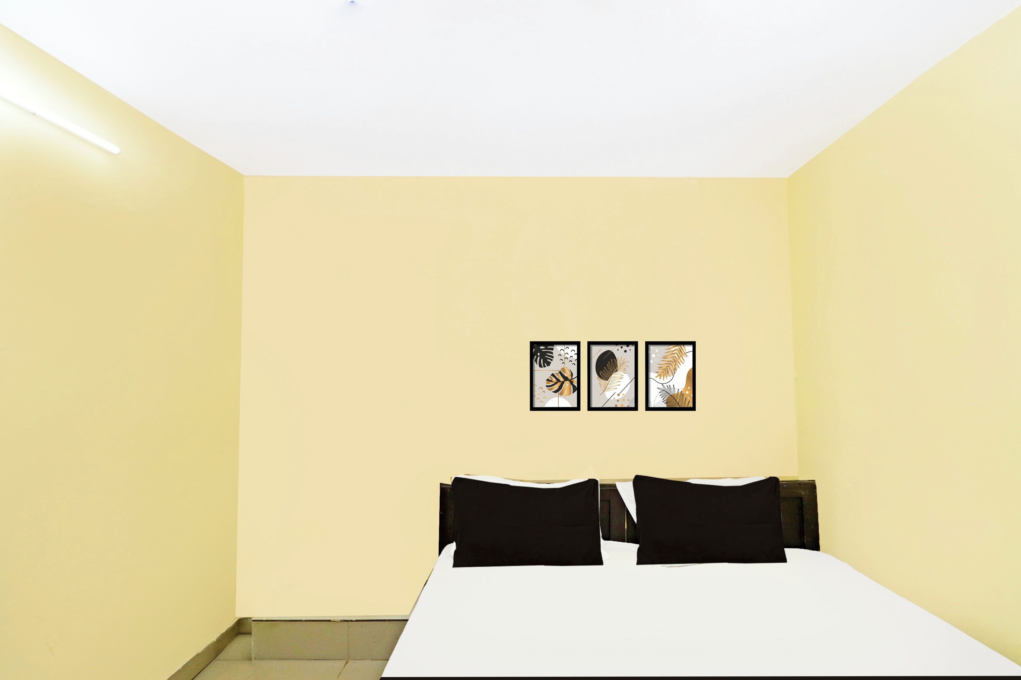 A room with a bed, a white table, and three framed artworks on the wall.
