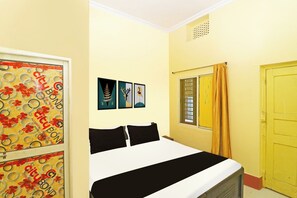 Habitació amb un llit, una finestra amb cortines i una porta. Hi ha tres quadres a la paret.