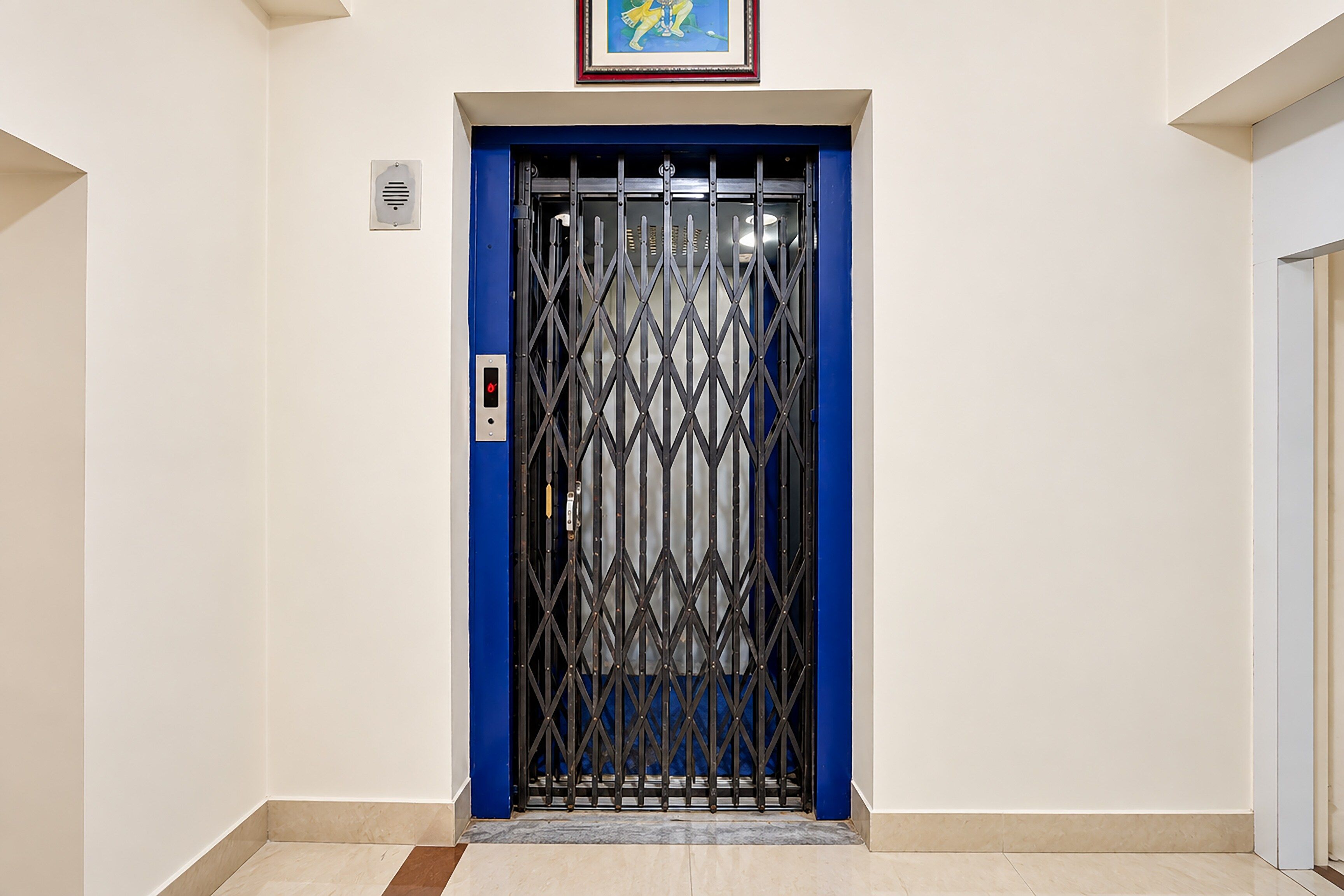 A blue elevator door with a metal security gate, a small sign above it, and a tiled floor.