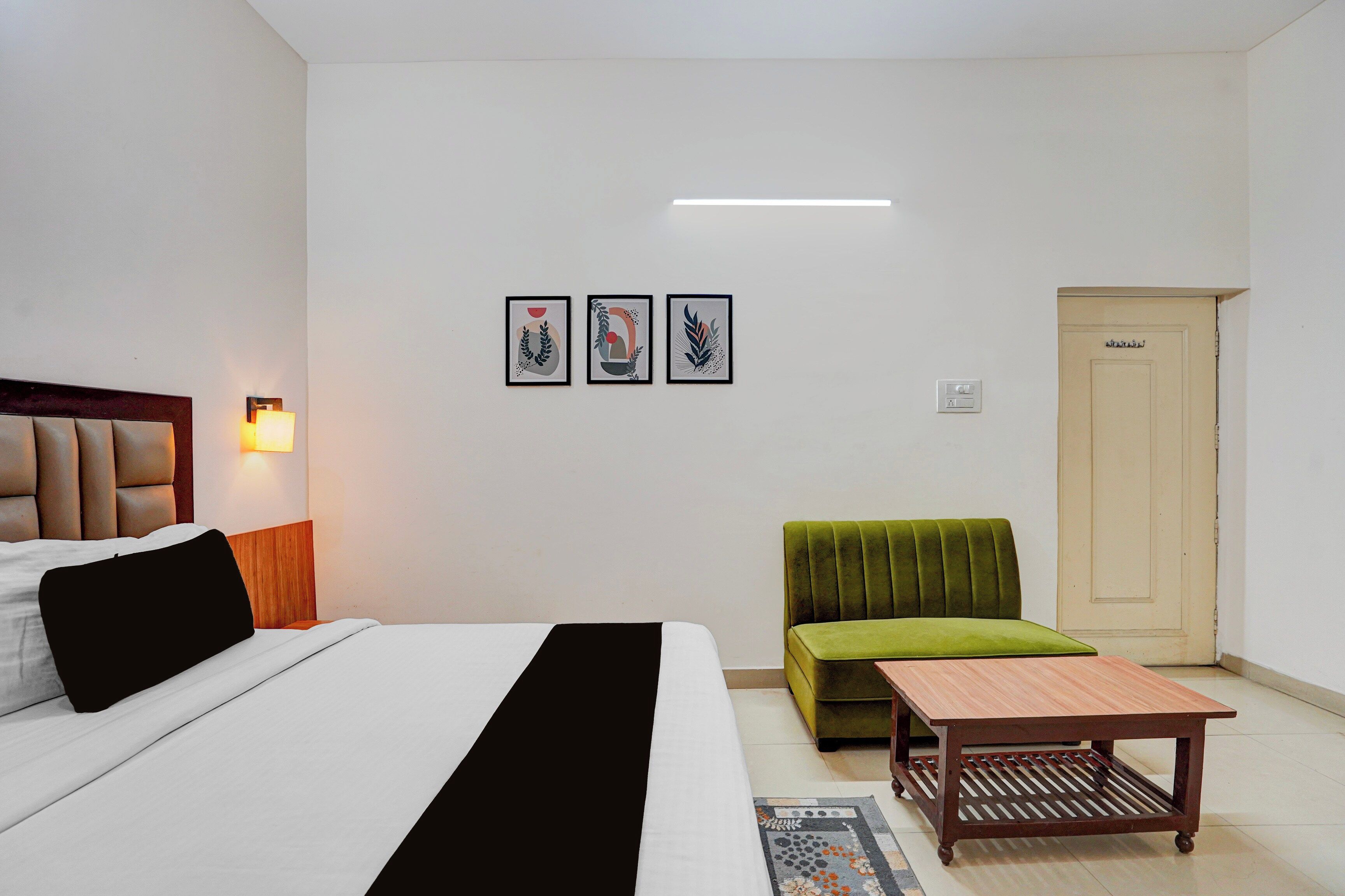A hotel room with a bed, a sofa, a small table, and a door. There are three framed pictures on the wall.