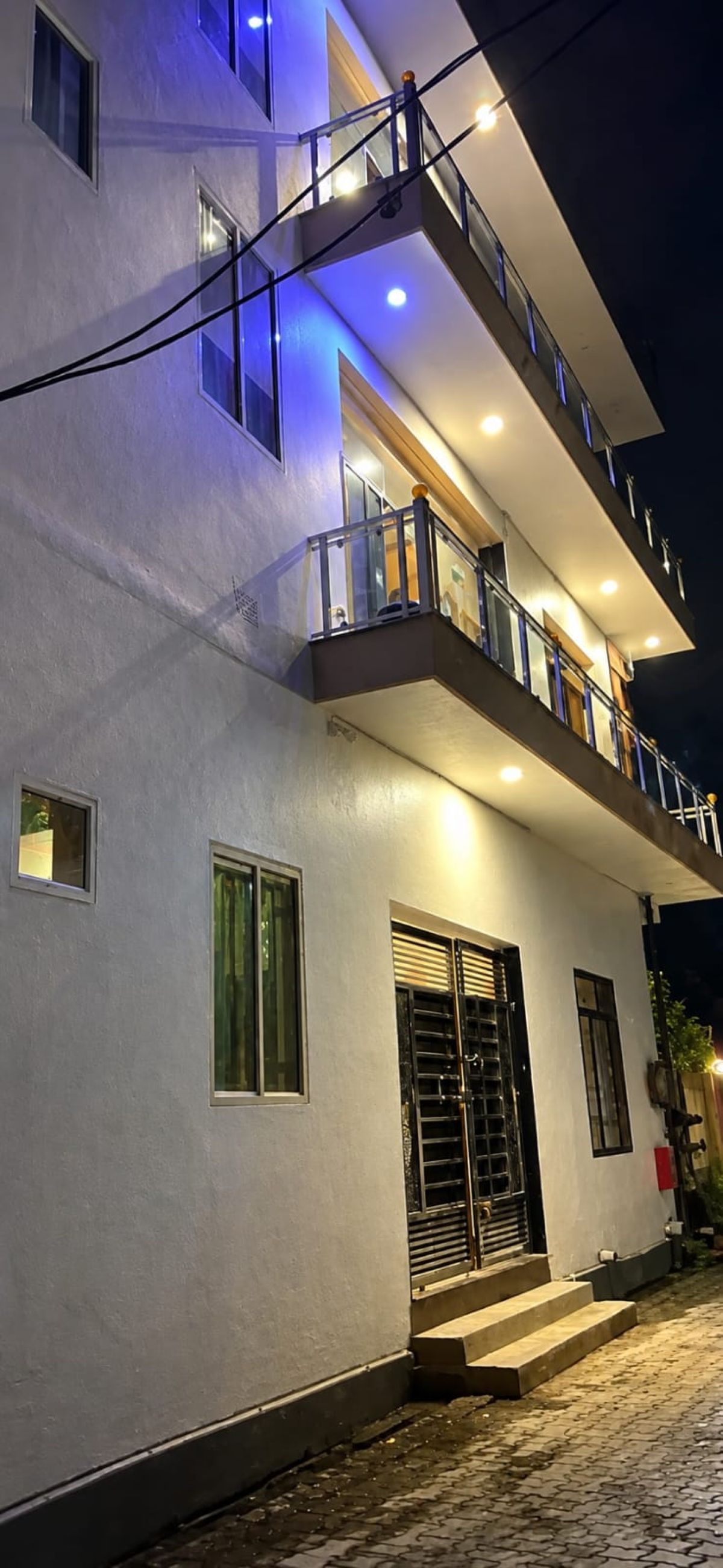 A multi-story building with a balcony on the upper floor, a set of stairs leading to the entrance, and a gated door.