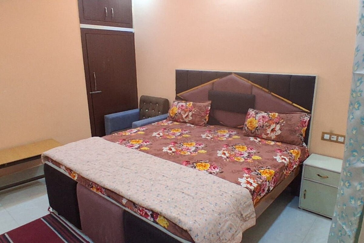 Quarto com cama, um banco, guarda-roupa e mesa de cabeceira.
