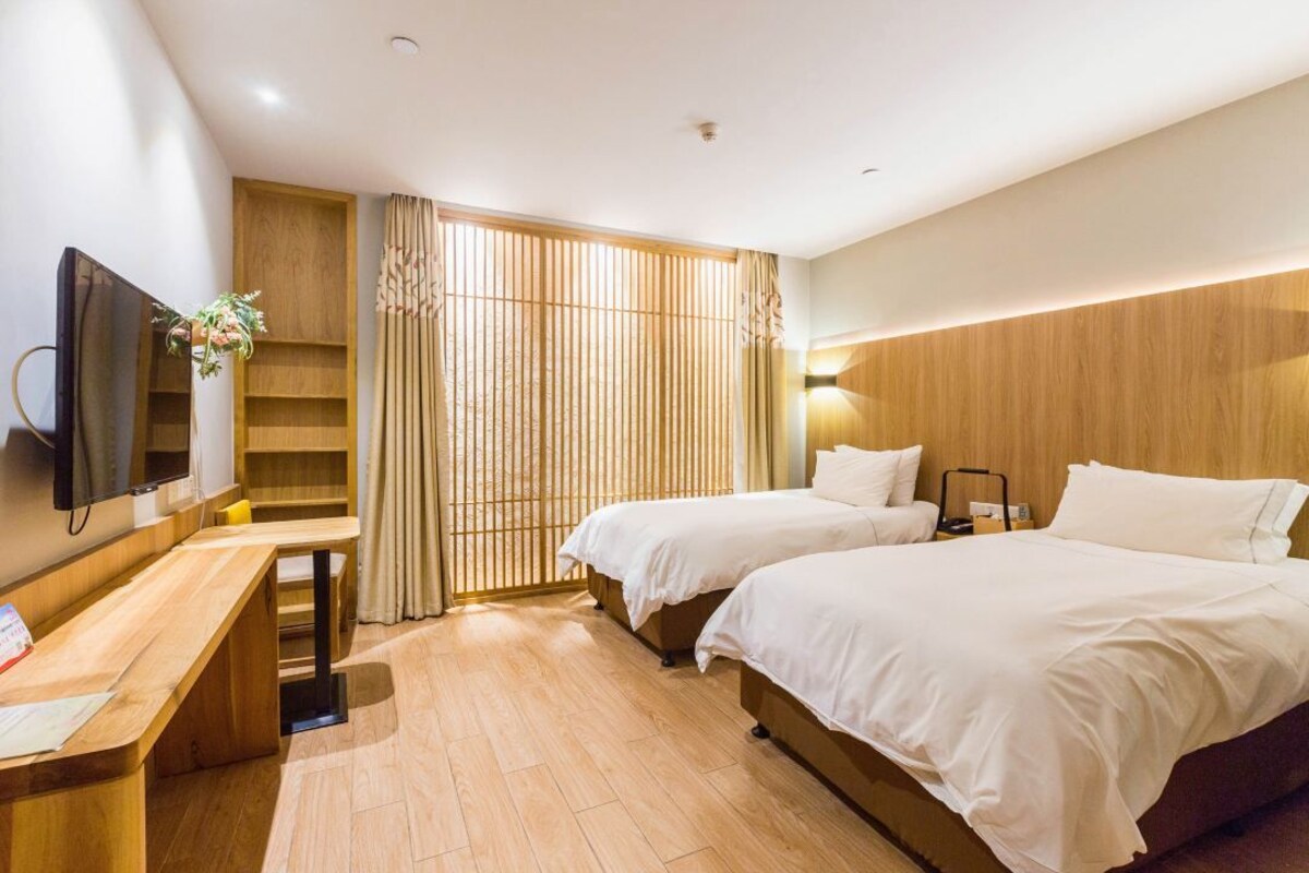 Quarto de hotel com duas camas, uma escrivaninha, televisão e uma porta de correr com cortinas.