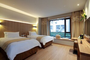 Quarto de hotel com duas camas, cabeceira de madeira, uma janela grande com vista e uma mesinha com um vaso de flores.