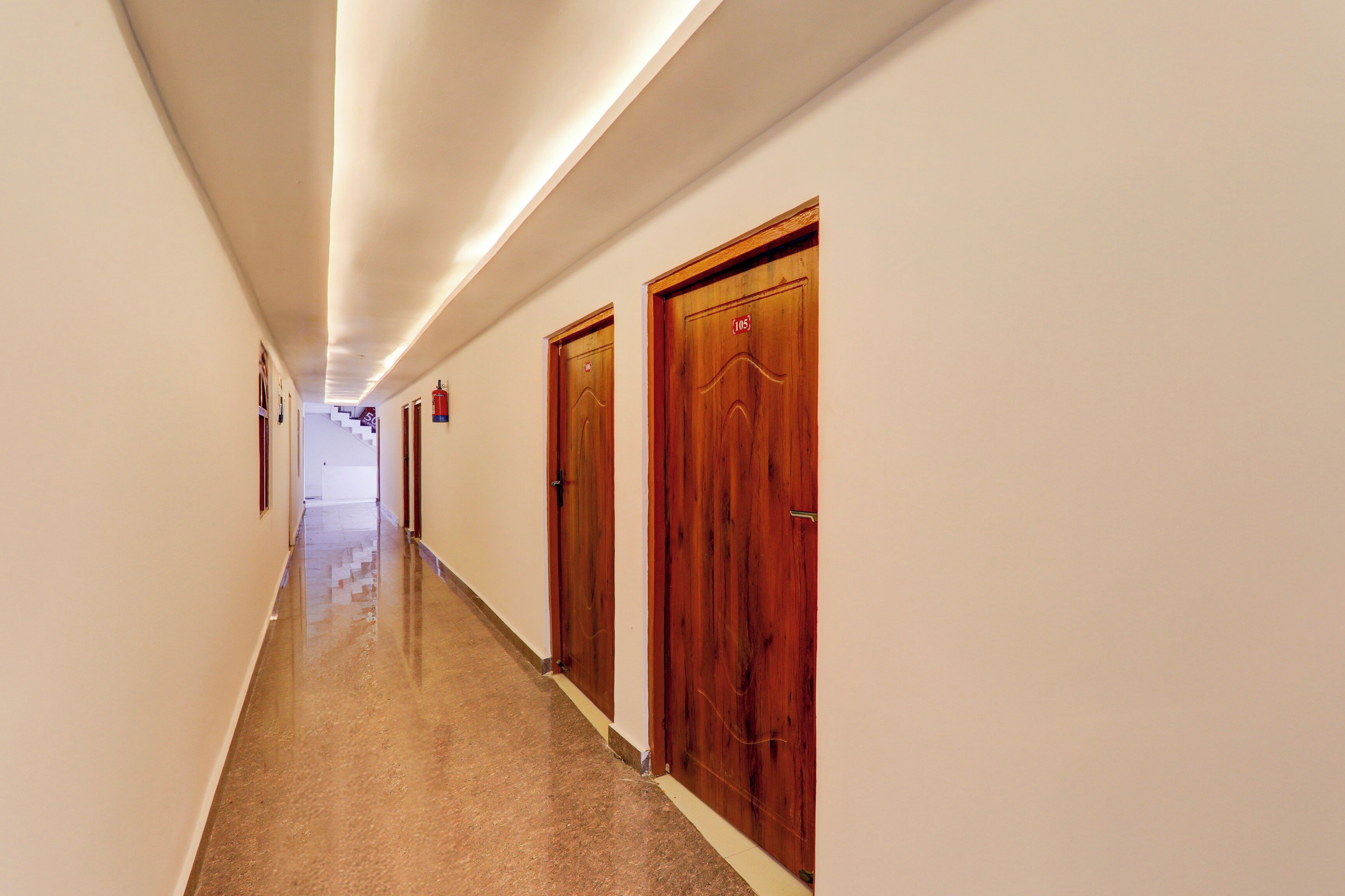 Un long couloir étroit, avec des portes en bois d ’un côté et un extincteur fixé au mur.