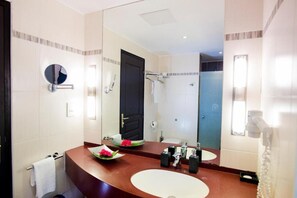 A modern bathroom with a large mirror, two sinks, a towel rack, and a shower area. - Mantis Soanambo Hotel and Spa Sainte Marie (Nosy Boraha)