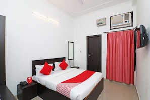 Habitación de hotel con una cama, un teléfono en la mesita de noche, una colcha de cuadros blancos y rojos, una cortina roja y un televisor montado en la pared.