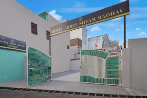 Entrada de un hotel con un letrero que dice 'Hotel Shree Shyam Madhav' y un camino de acceso con portones.
